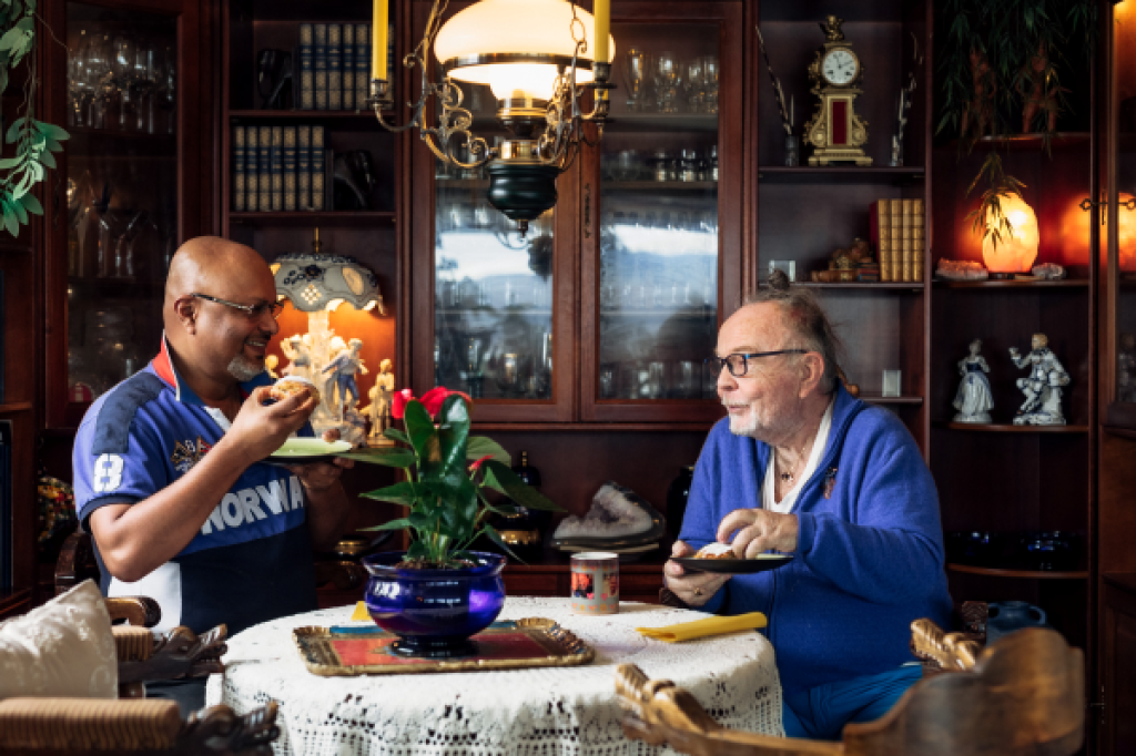 To eldre menn sitter ved et bord og spiser