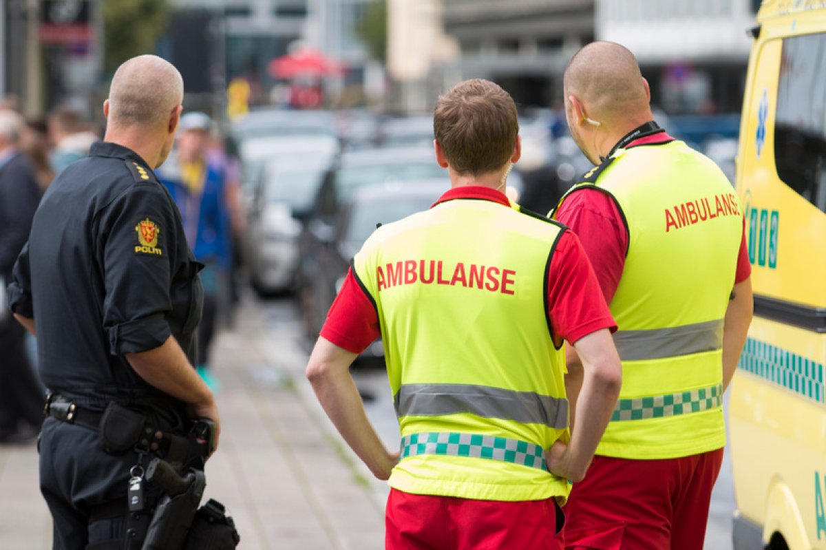 en politimann og to ambulansearebeidere på fortauet ved siden av en ambulanse